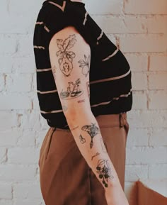 a woman with a tattoo on her arm and shoulder standing in front of a brick wall