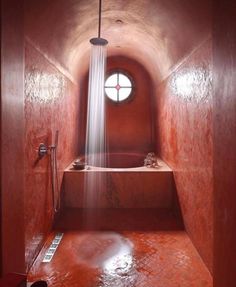 a red bathroom with a round window in the corner and a shower head on the wall