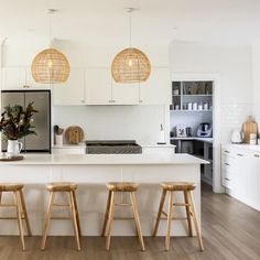 three stools sit in front of an island with white countertops and cabinets, along with hanging lights