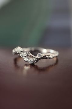 a white gold wedding band with leaves and diamonds on top of a wooden table in front of a blurry background