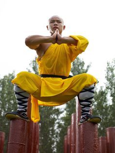 a man in yellow shirt and black pants standing on poles with his hands behind his head