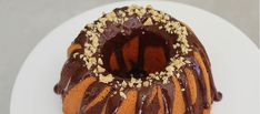 a bundt cake with chocolate icing and nuts on top sitting on a white plate