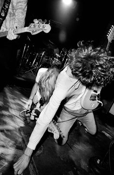 black and white photograph of two people playing guitar on stage with guitars in the background