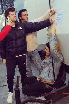 three men standing next to each other near a white truck and talking on the phone