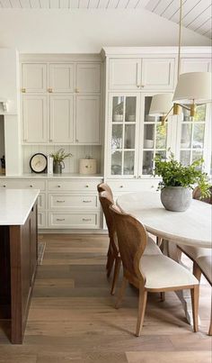 a large kitchen with white cabinets and wooden flooring, along with a dining table