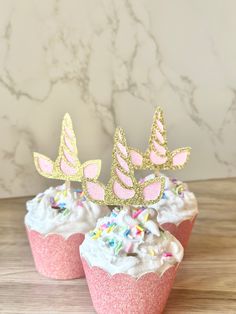 two cupcakes with pink frosting and gold glitter crowns on top are sitting on a table