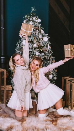 two beautiful young women standing in front of a christmas tree holding up boxes with presents