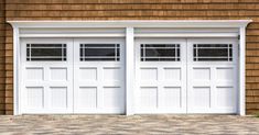 two white garage doors on the side of a brown building with brick flooring and windows