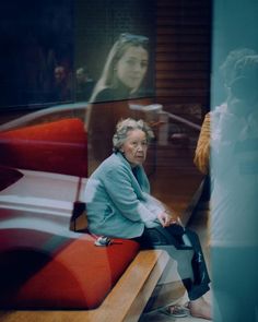 an older woman sitting on a bench in front of a glass window with her reflection