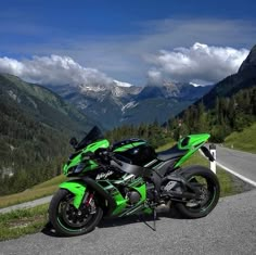 a green motorcycle parked on the side of a road near mountains and clouds in the sky