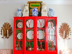 a red china cabinet with plates and vases on top