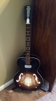 a black guitar sitting on top of a floor next to a wooden cabinet and door