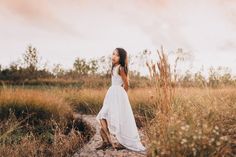 a woman in a white dress walking through tall grass