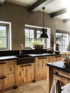 a kitchen with wooden cabinets and black counter tops, potted plants on the window sill