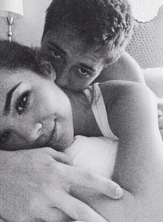 a black and white photo of two people cuddling on a bed with one woman's head resting on the pillow