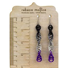 pair of purple and black earrings with silver chain attached to hooks, on wooden ruler