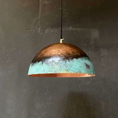 a copper and turquoise colored pendant light hanging from a metal ceiling fixture against a gray wall