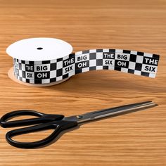 a pair of scissors next to a black and white checkered ribbon on a wooden table