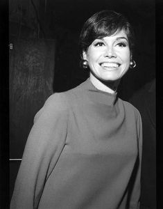 black and white photograph of woman smiling at camera with man in background behind her wearing suit