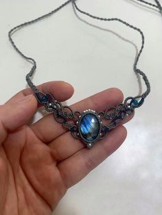 a hand holding a necklace with a blue stone in it's center and an intricate design on the front