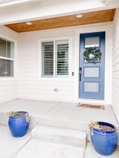 two blue planters sitting on the front steps of a white house with a blue door