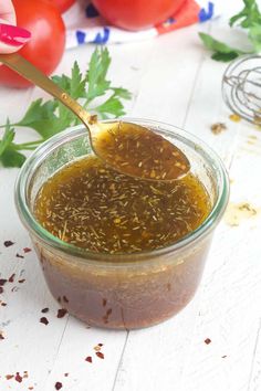 a spoon full of sauce sitting on top of a table next to tomatoes and parsley