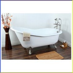 a white bath tub sitting on top of a wooden floor next to a vase with flowers