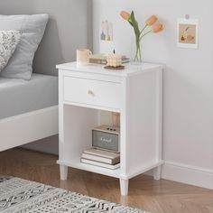 a white nightstand table with flowers and books on it