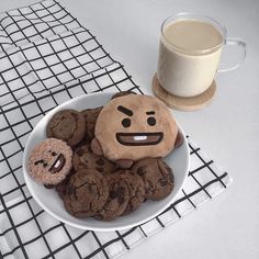 a plate full of cookies with faces drawn on them next to a glass of milk