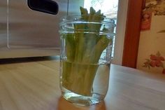 a glass jar filled with green onions sitting on top of a wooden table