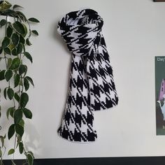 a black and white scarf hanging on a wall next to a plant with green leaves