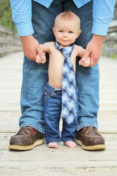 a baby wearing a tie is being held by his dad's hands as they stand on a bridge