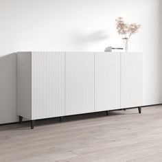 a white cabinet sitting on top of a hard wood floor next to a plant in a vase