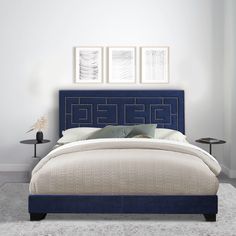 a bed with blue upholstered headboard in a white walled room, and three framed pictures on the wall above it