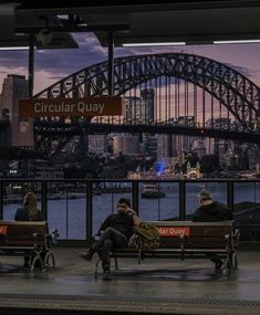 people sitting on benches in front of the sydney harbour bridge