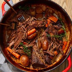 pot roast with carrots, potatoes and meat in a red pan on a wooden table