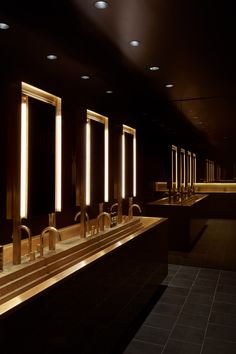 a row of sinks in a dark room with lights on the walls and below them