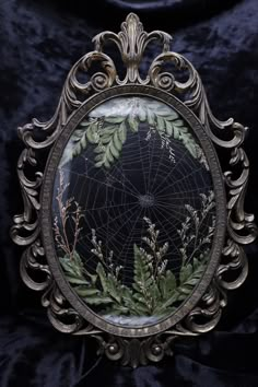 an ornate mirror with leaves and spider web in the center on a black velvet background