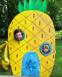 two children are smiling in front of a large pineapple shaped house made out of cardboard