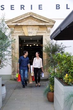 a man and woman walking out of a building holding shopping bags in their hands,