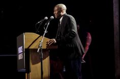 a man standing at a podium in front of a microphone and speaking into a mic