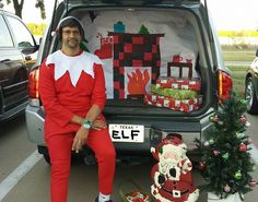 a man dressed as elf sitting in the back of a car next to christmas decorations