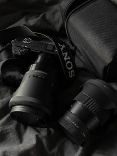 two cameras sitting next to each other on top of a bed with a black bag