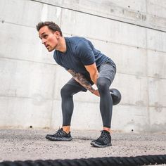 a man doing squats with a kettle in front of a concrete wall and black rope