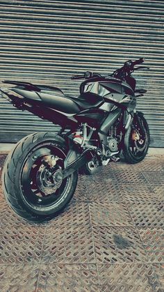 a black motorcycle parked in front of a garage door next to a brick sidewalk and wall