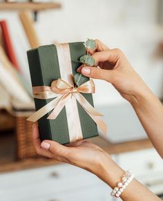 a woman is holding a green and white gift box with a bow on it's side