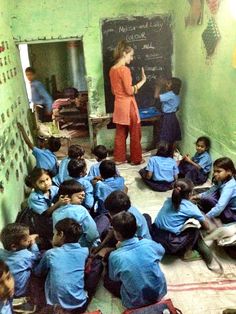 a group of children sitting on the floor in front of a blackboard with writing on it