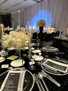 a table set with black and white place settings, silverware, flowers and candles