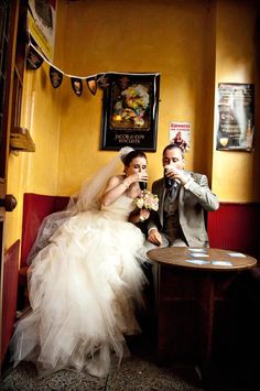 a bride and groom sitting at a table in front of a wall with pictures on it