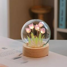 there is a glass ball with flowers in it sitting on a table next to an open book